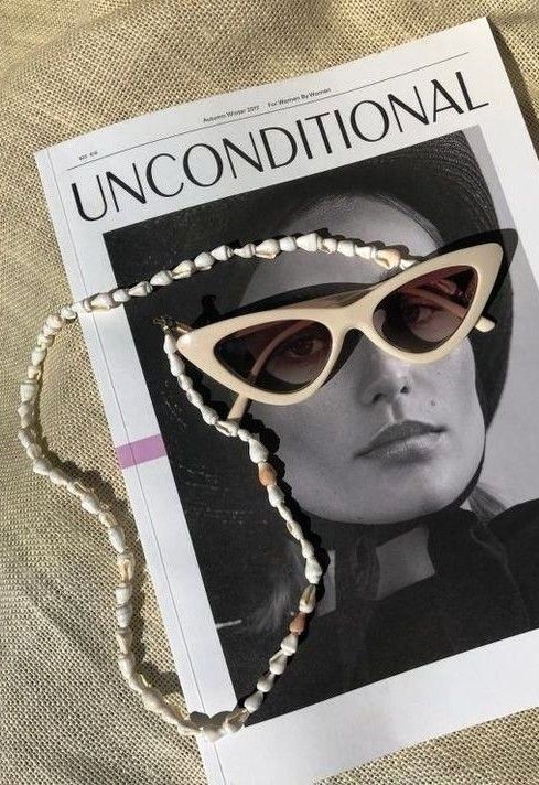 Flat lay con estética editorial y retro:gafas blancas estilo 60s con cadena de pequeñas conchas.